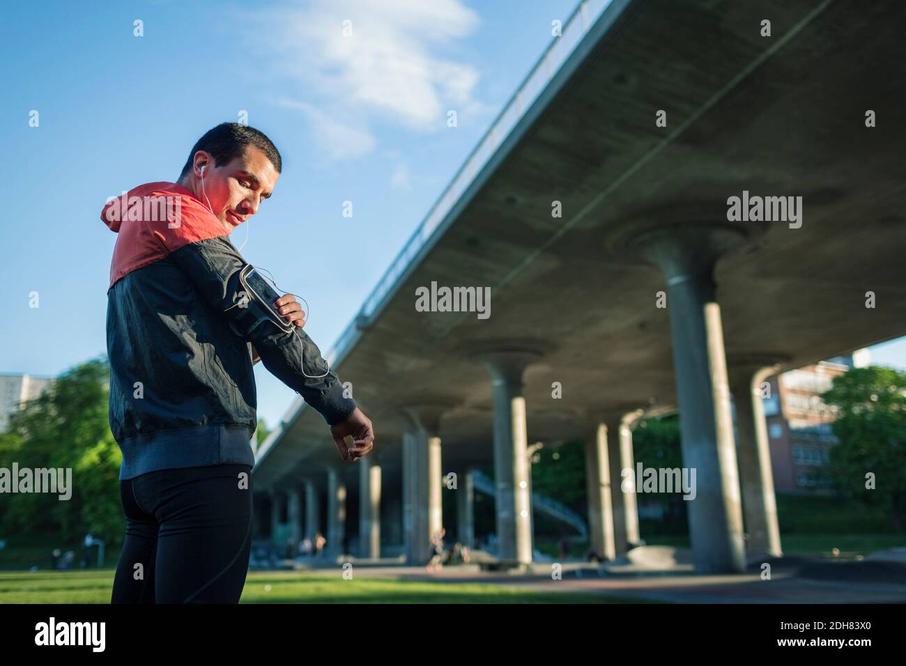 Low angle view of man touching arm band while standing against bridge Stock Photo