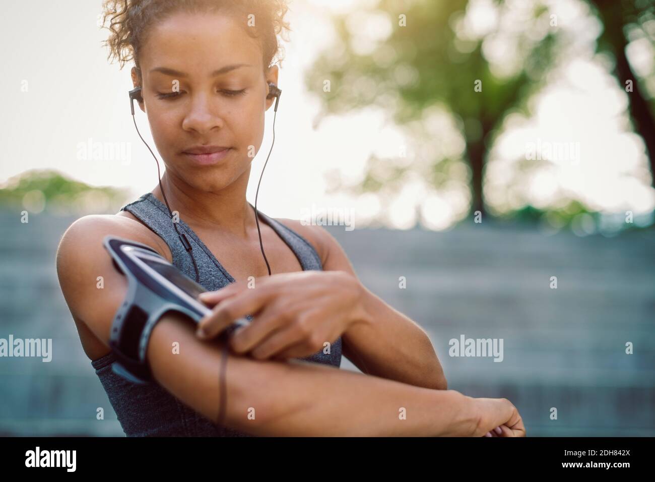 Woman using smart phone armband while standing at park Stock Photo