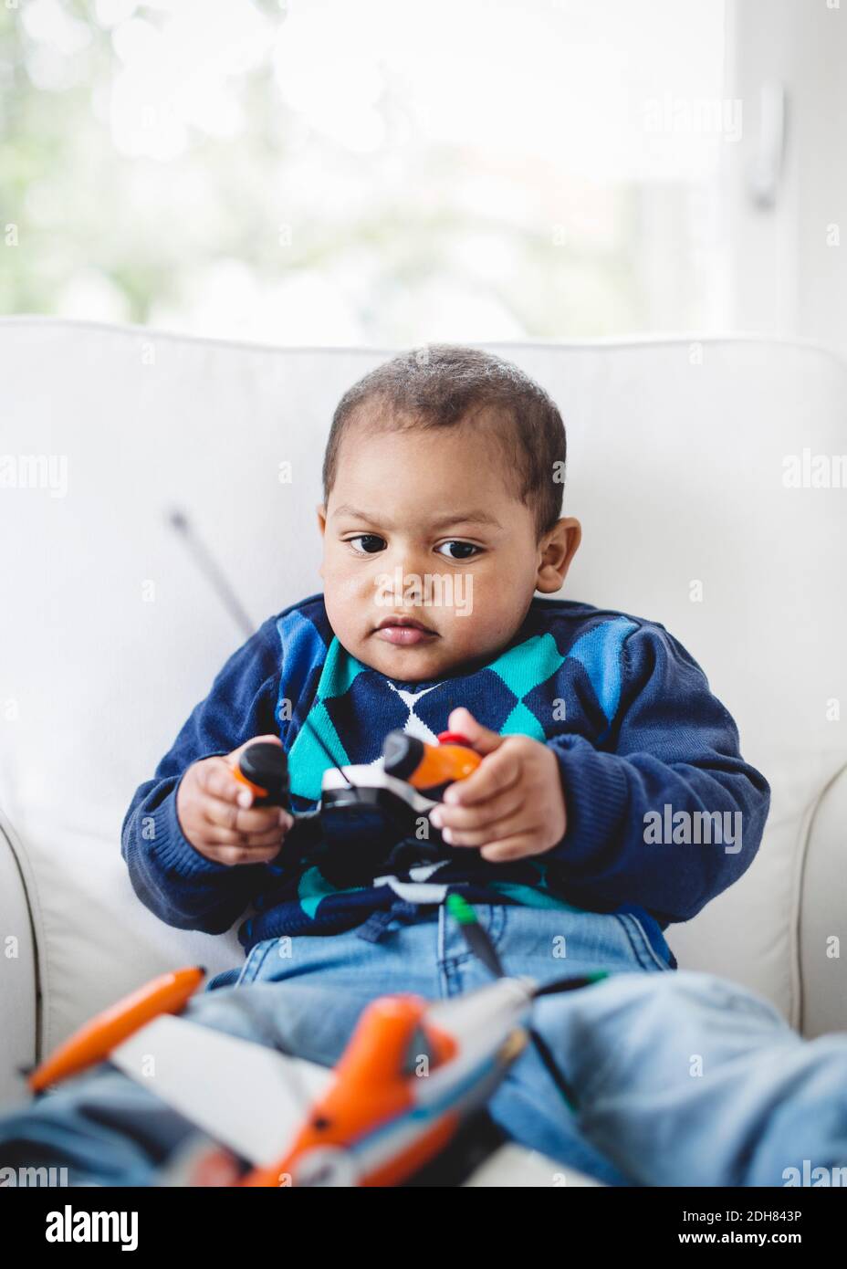 Boy playing with remote controlled airplane on armchair at home Stock Photo