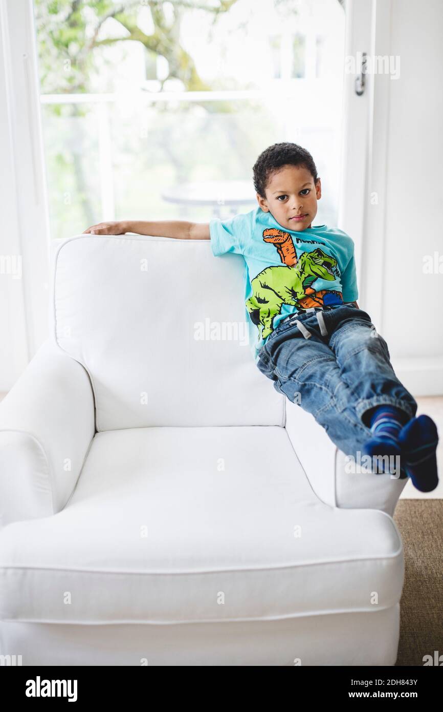 Portrait of boy sitting on handrest of armchair at home Stock Photo
