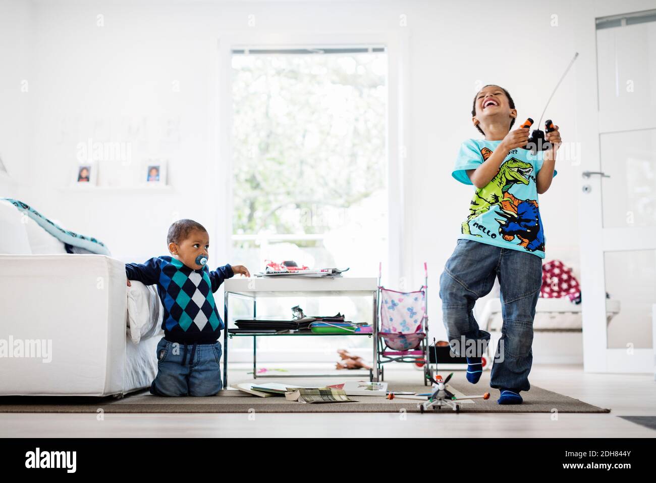 Boy looking at happy brother holding remote of model airplane at home ...