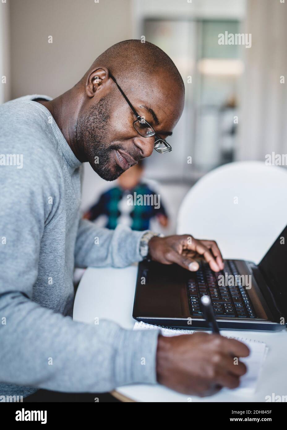 Side view of man writing while working on laptop at home Stock Photo