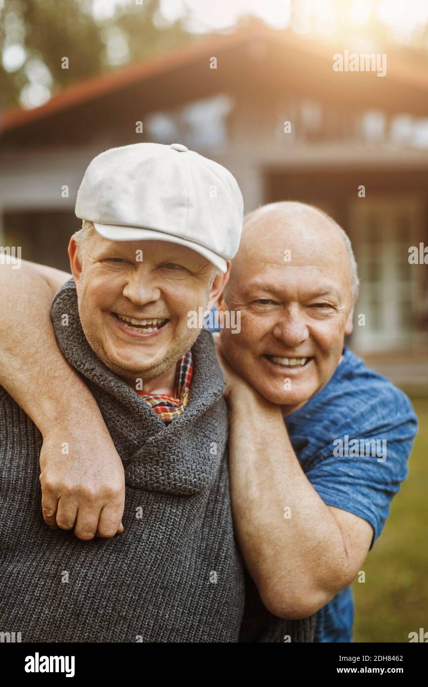 Portrait of happy gay man leaning on partner's shoulders at yard Stock Photo