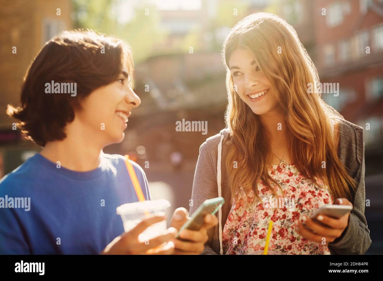 Happy teenagers looking at each other while holding smart phones outdoors Stock Photo