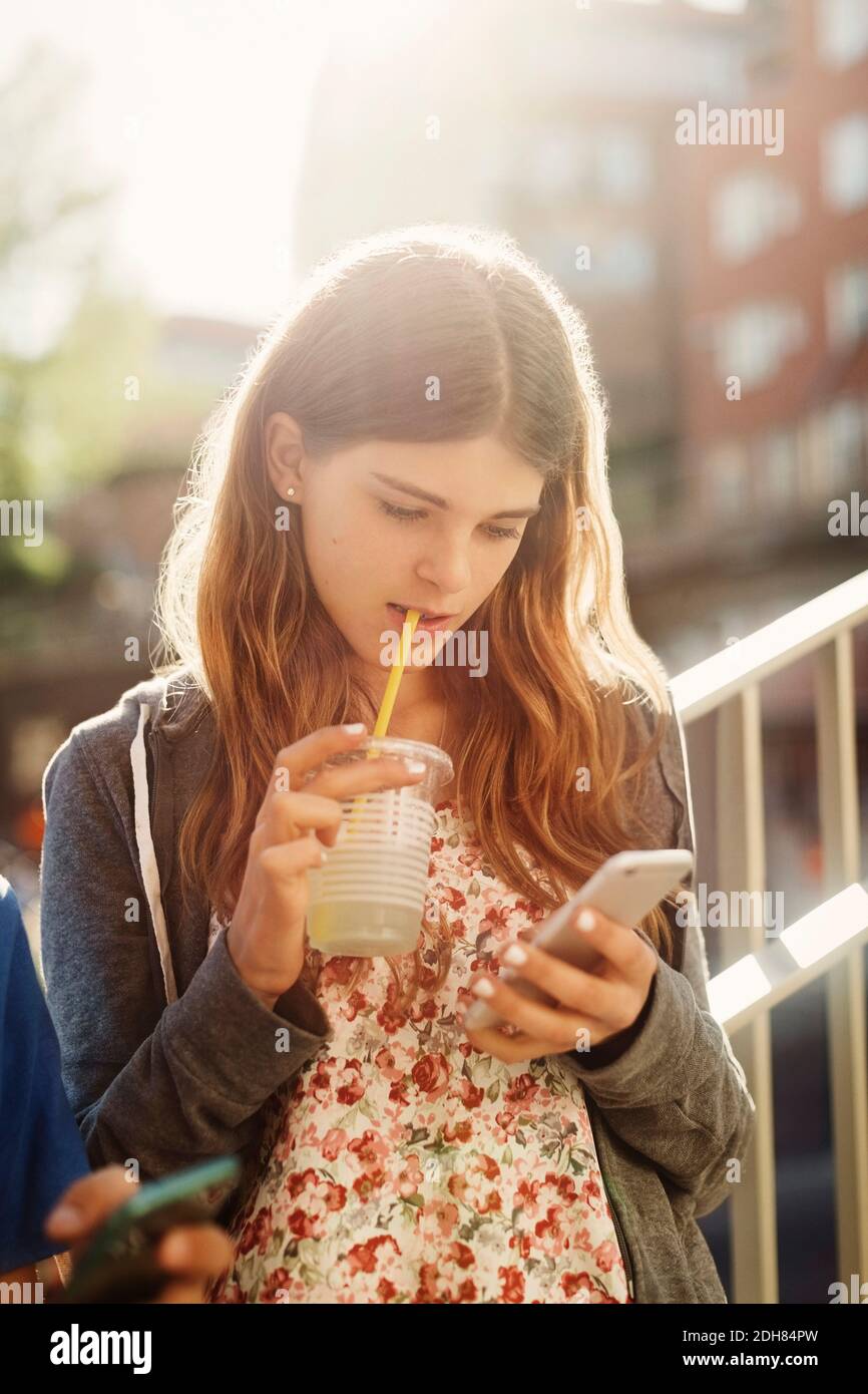 Female teenager using smart phone while drinking juice outdoors Stock Photo