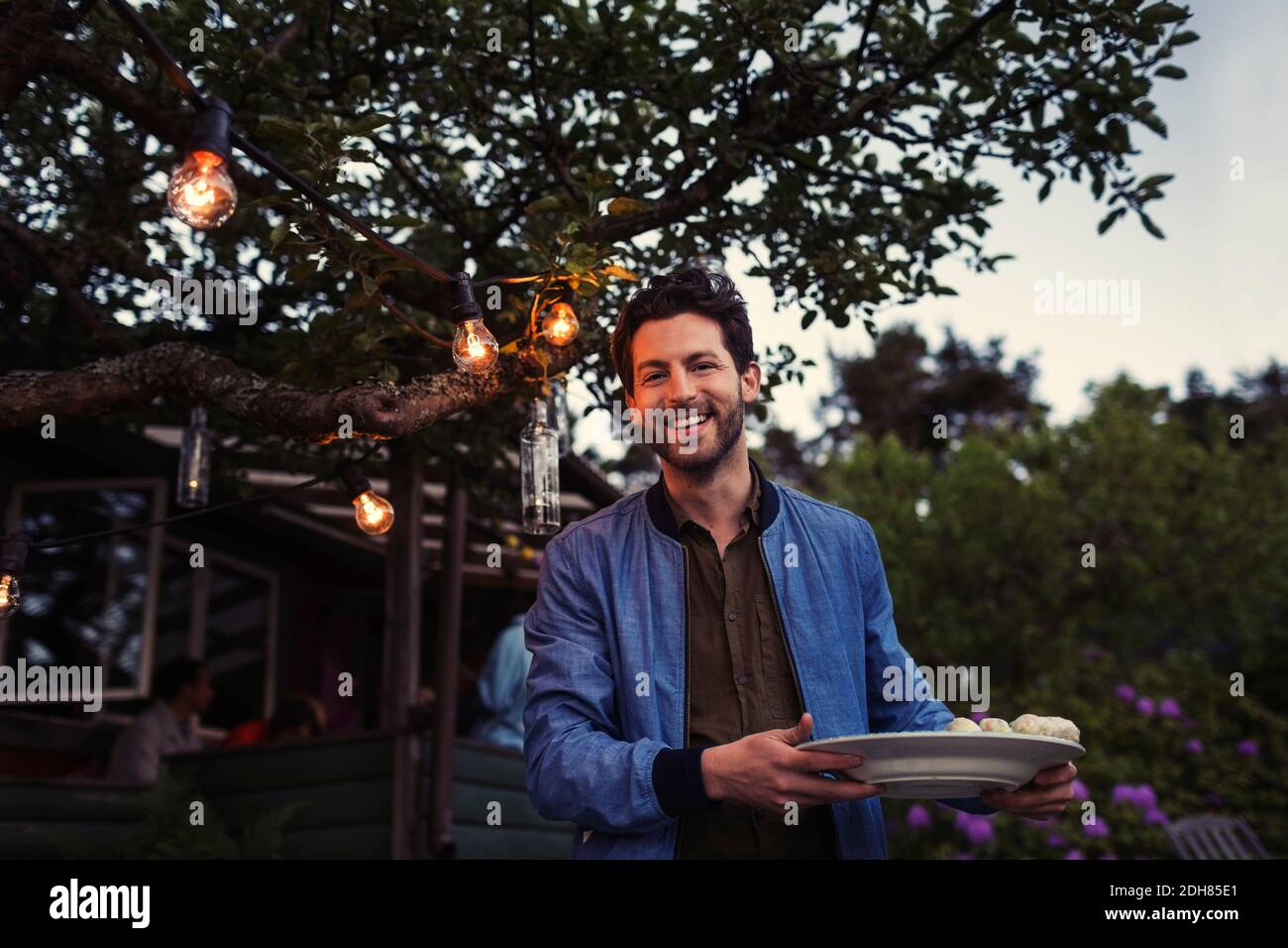 Portrait of happy man holding plate while standing at yard during dinner party Stock Photo