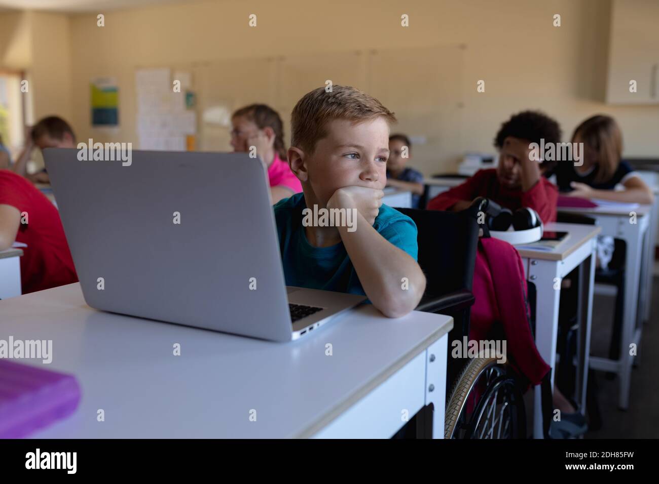 Schoolboy wearing glasses sitting at a desk using a laptop computer ...