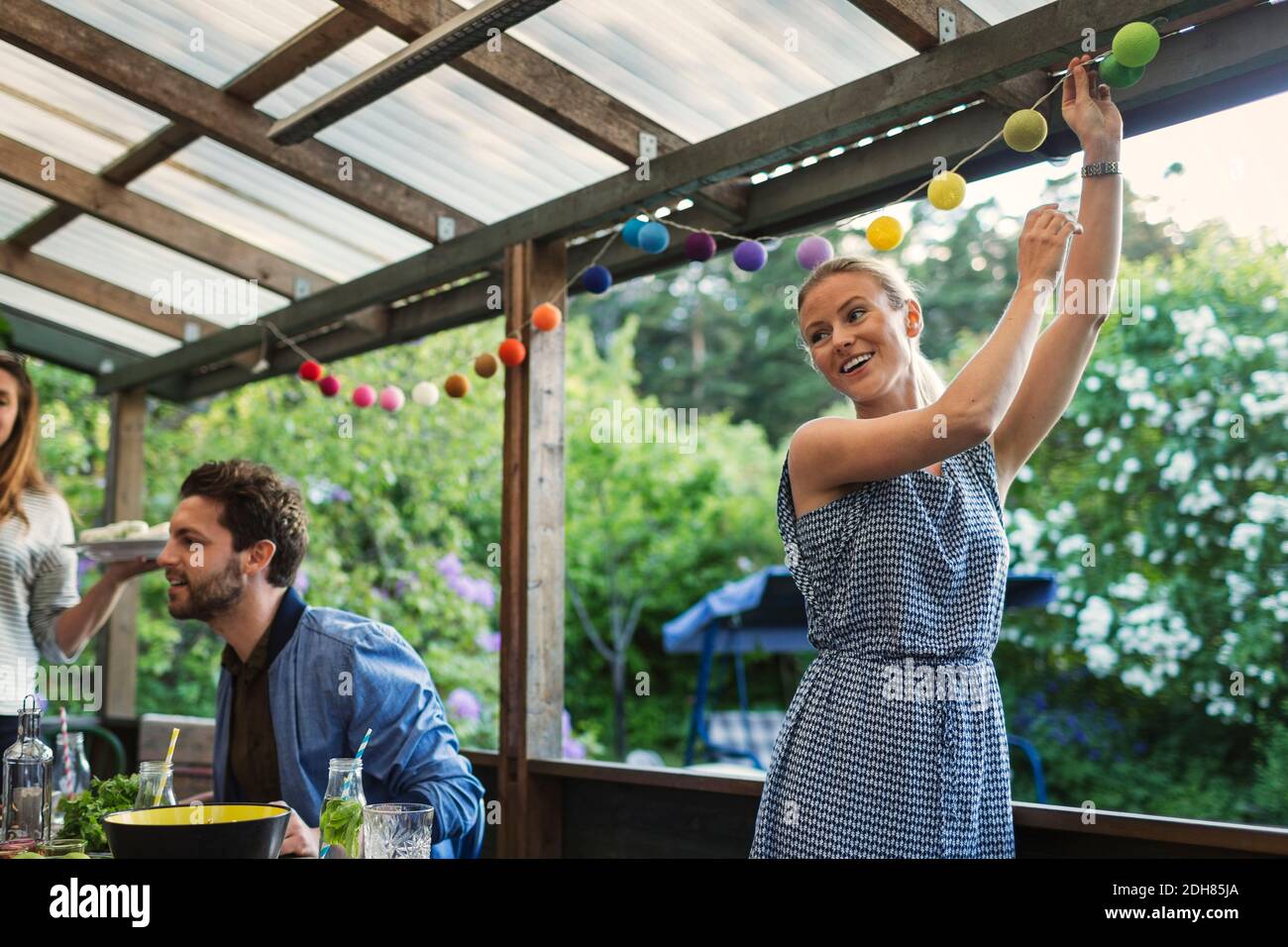 Happy young woman decorating log cabin during summer party with friends Stock Photo
