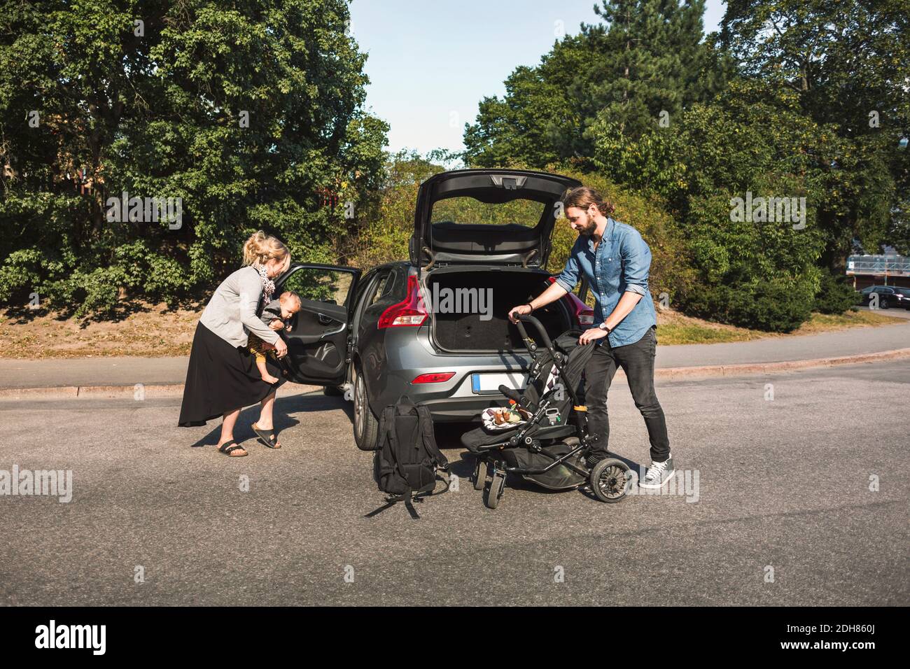 Mid adult parents with son and baby stroller near car on street Stock Photo