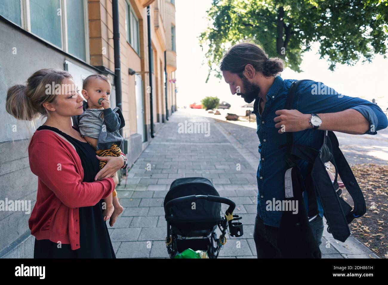 Mother with son looking at man wearing baby carrier on sidewalk Stock Photo
