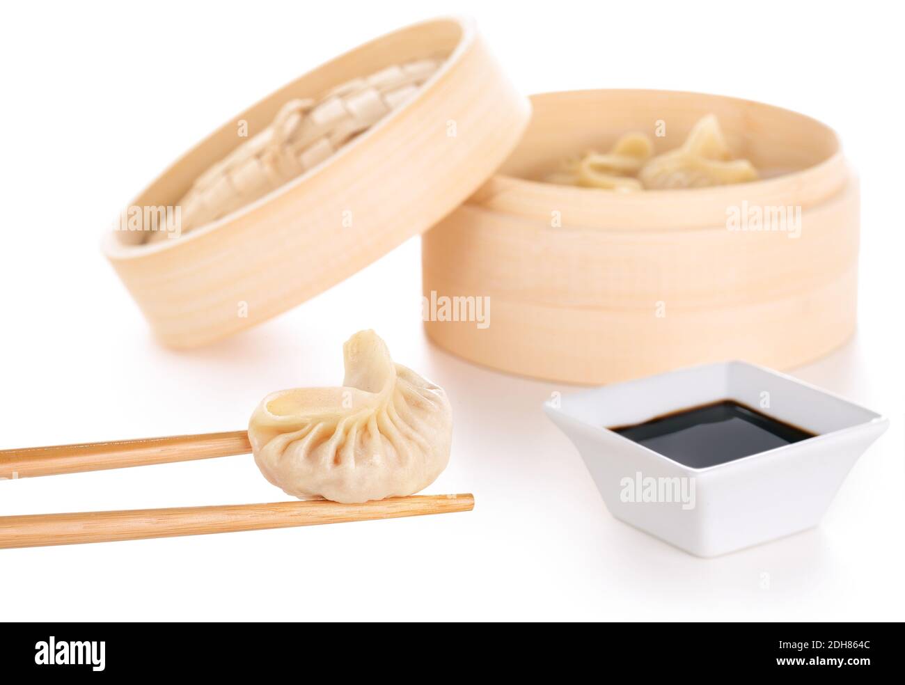 chopsticks holding a chinese dumpling, soy sauce and bamboo basket in white background Stock Photo