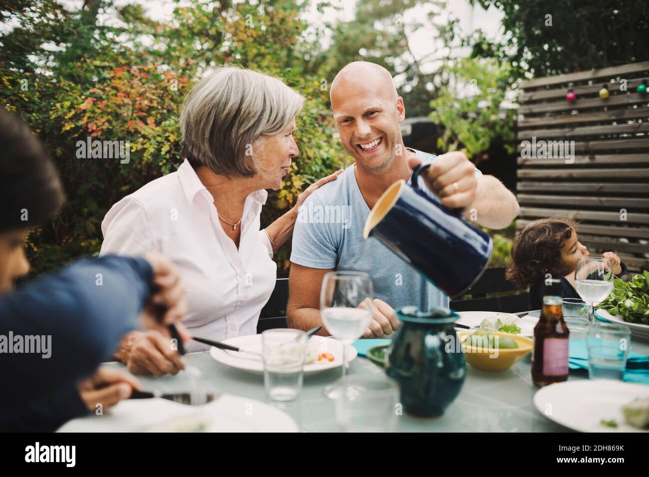 Happy man serving water to mother at outdoor dining table Stock Photo