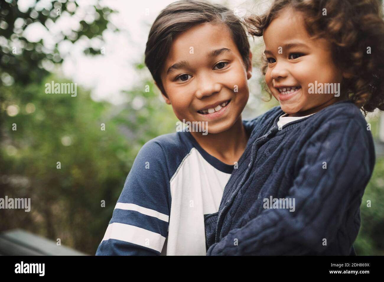 Portrait of happy boy carrying sister at yard Stock Photo