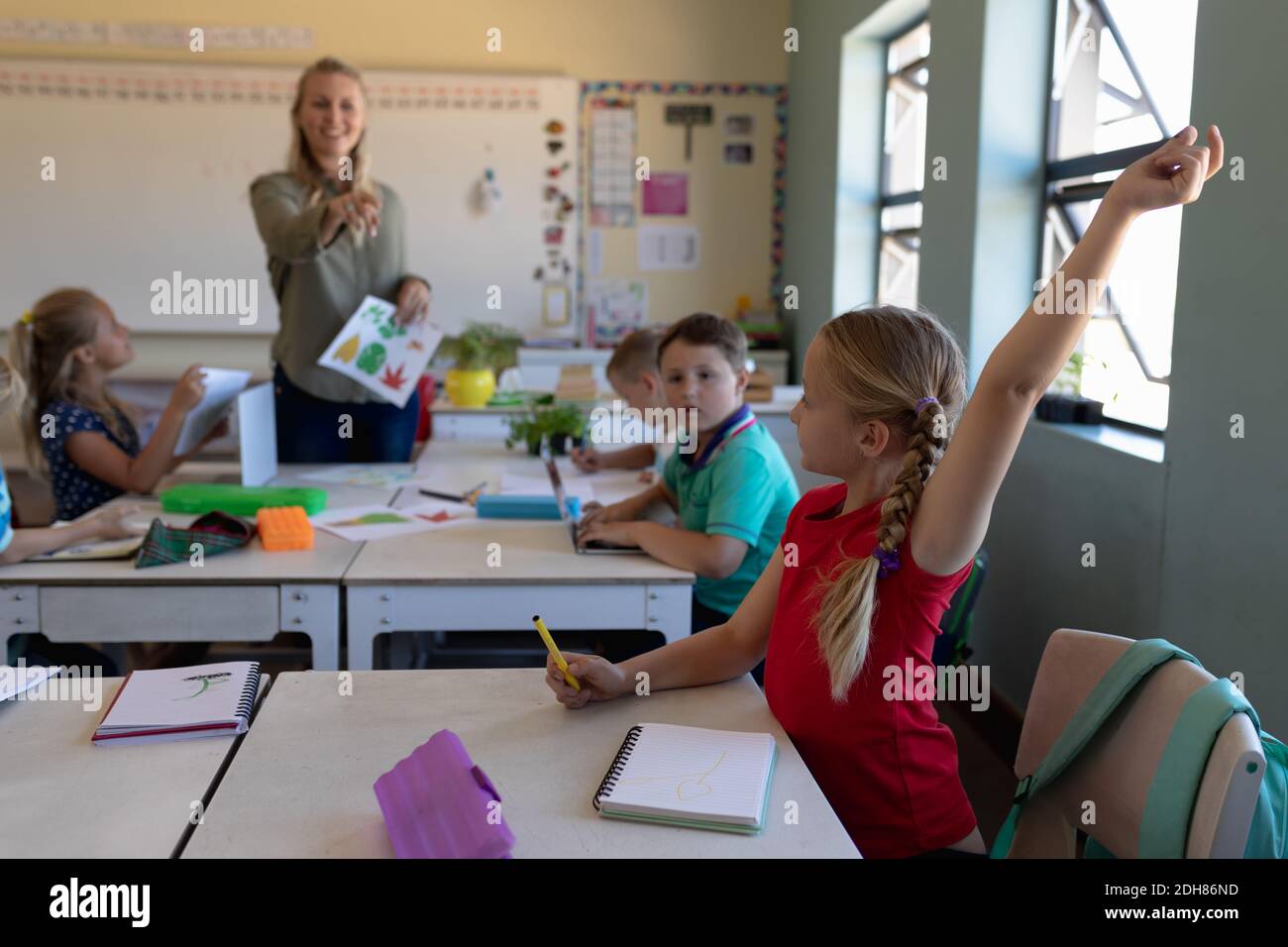 Schoolgirl sitting at a desk raising her hand in an elementary school ...
