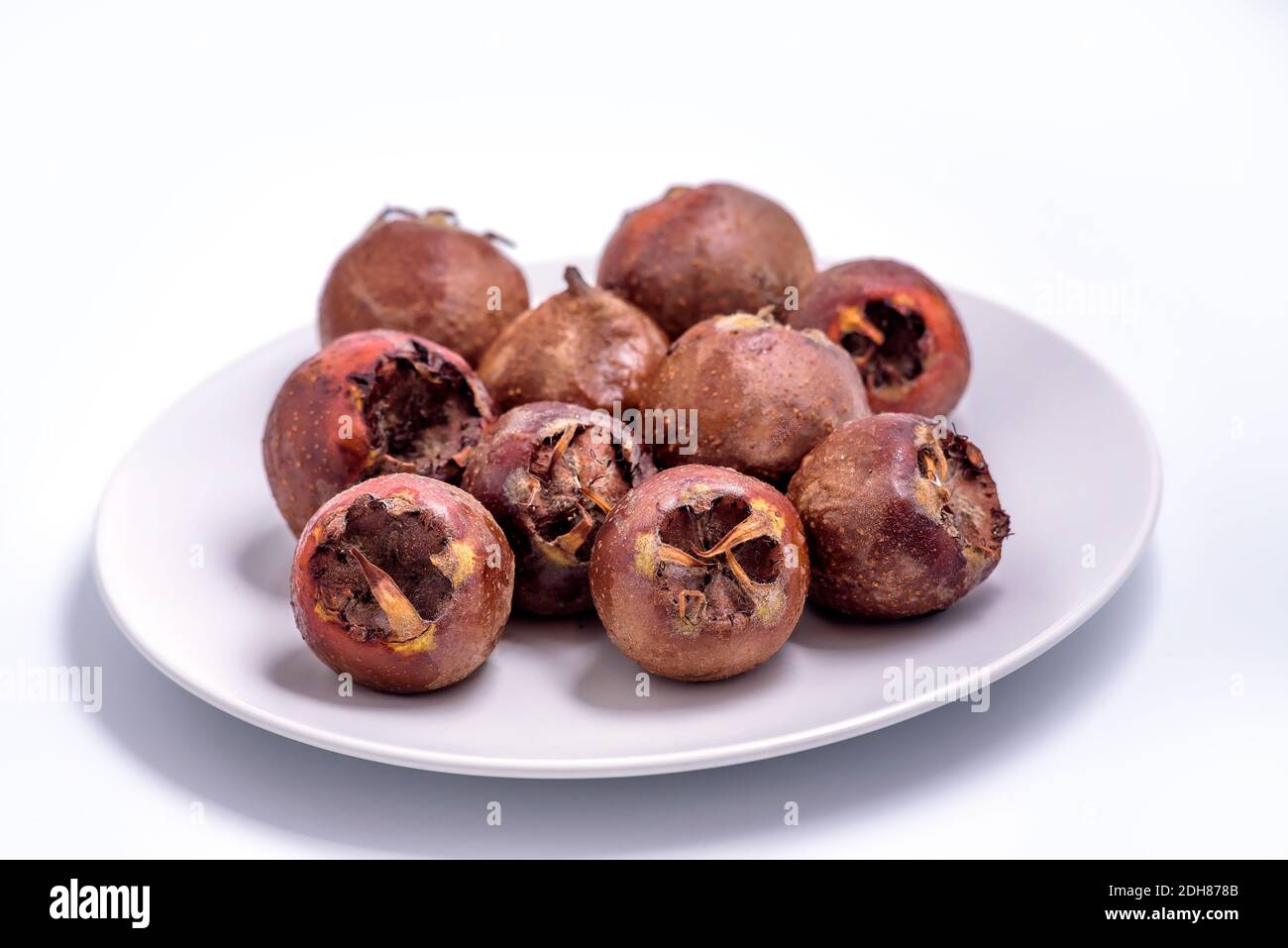 Fresh ripe organic common medlar fruit on a plate on white background. Healthy food Mespilus germanica Stock Photo