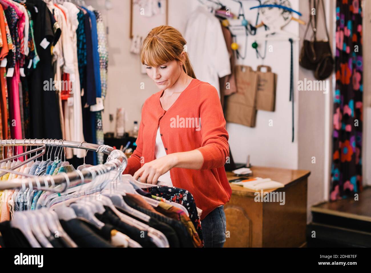 Owner arranging clothes on rack while standing at thrift store Stock Photo