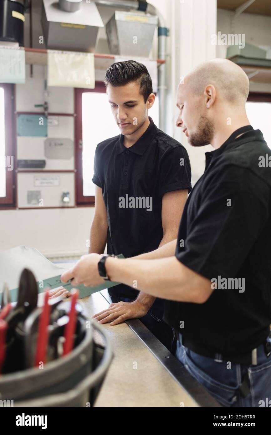 Teacher assisting male trainee over project in workshop Stock Photo