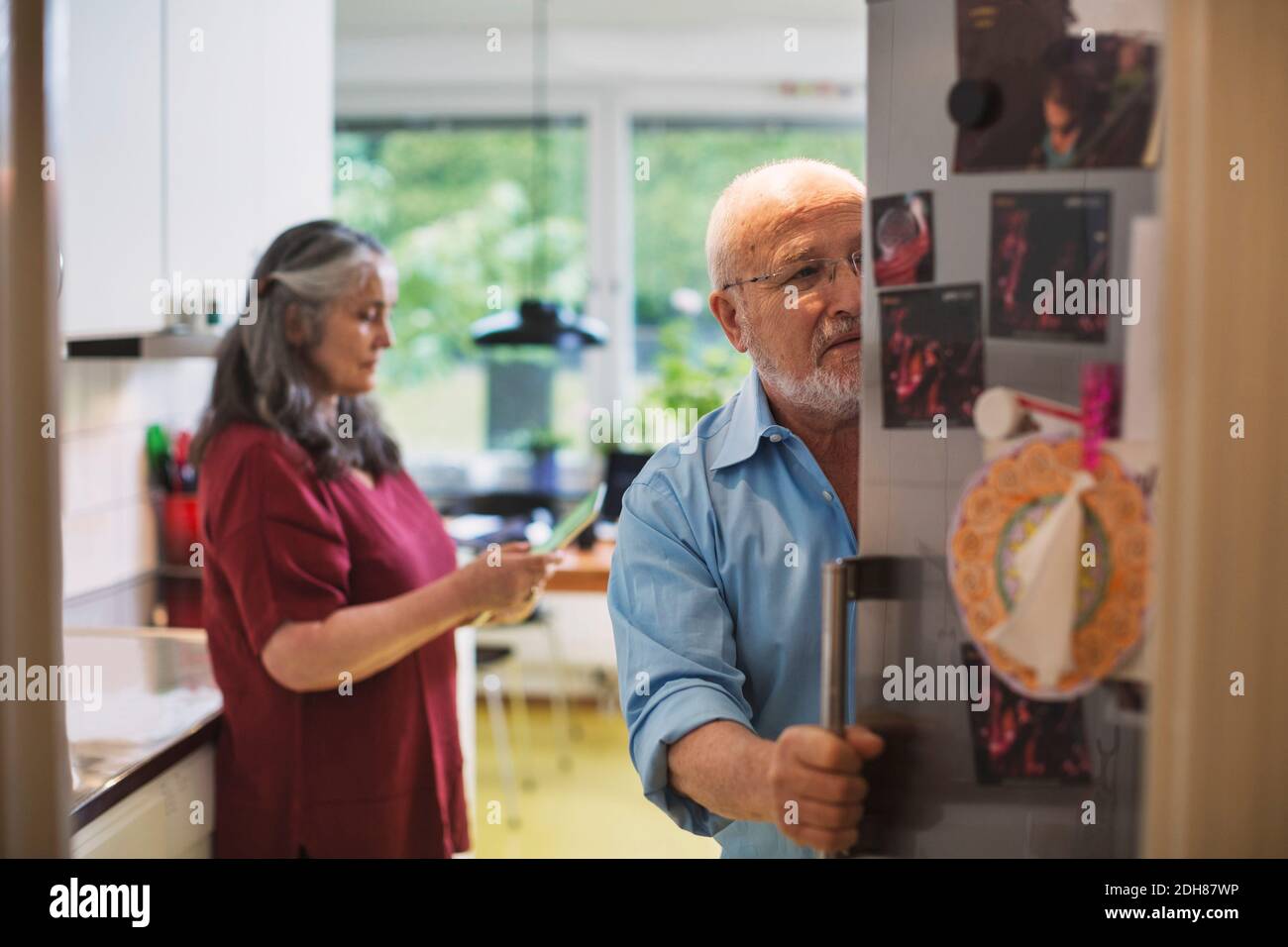 Senior man opening refrigerator while woman using digital tablet at home Stock Photo