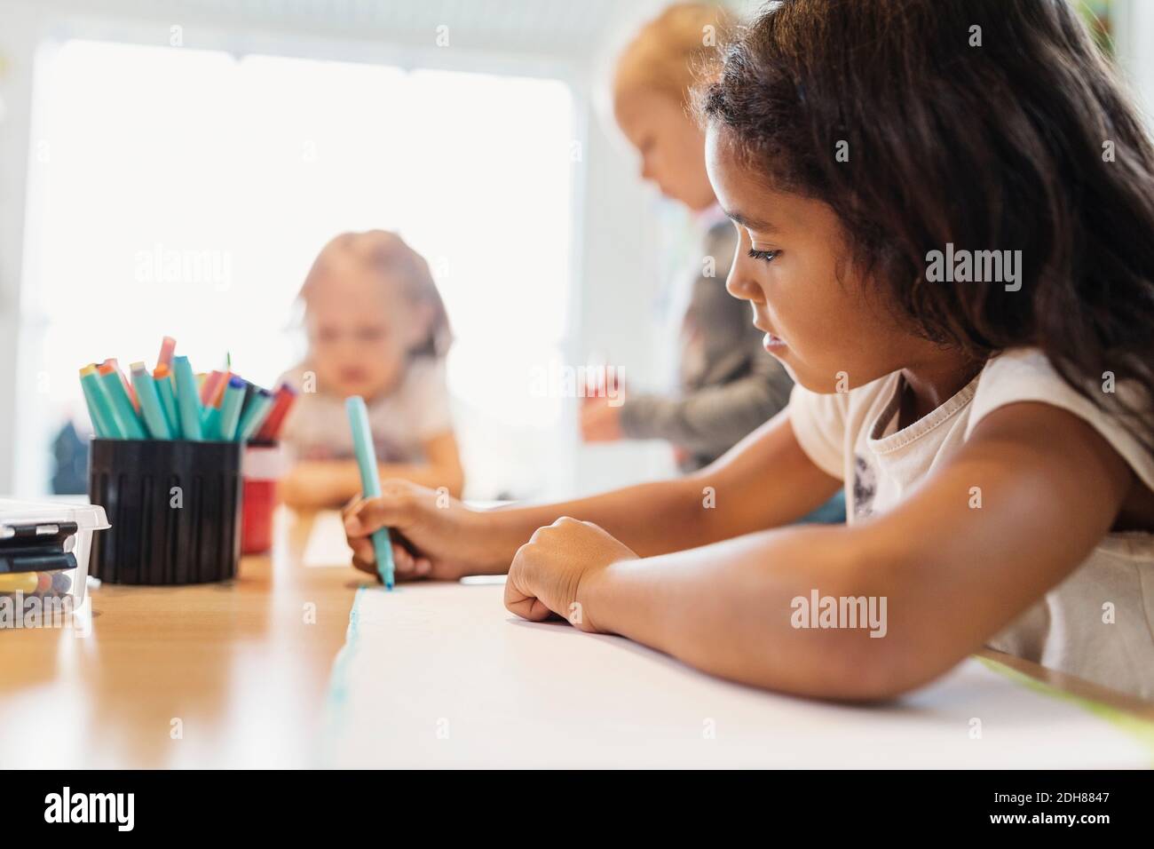 Girl using felt tip pen in drawing class with classmates in background Stock Photo