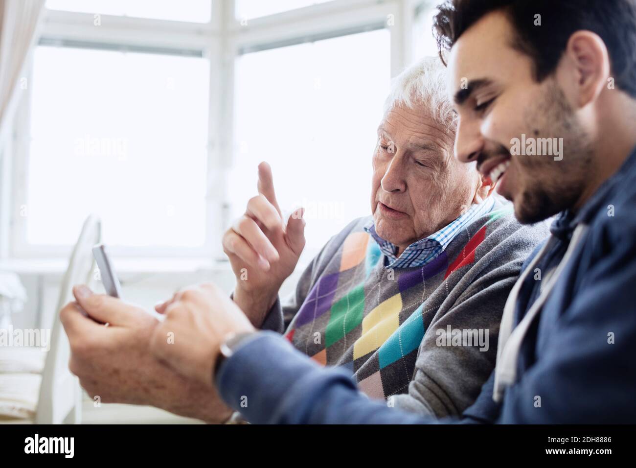 Caretaker assisting man in using mobile phone at nursing home Stock