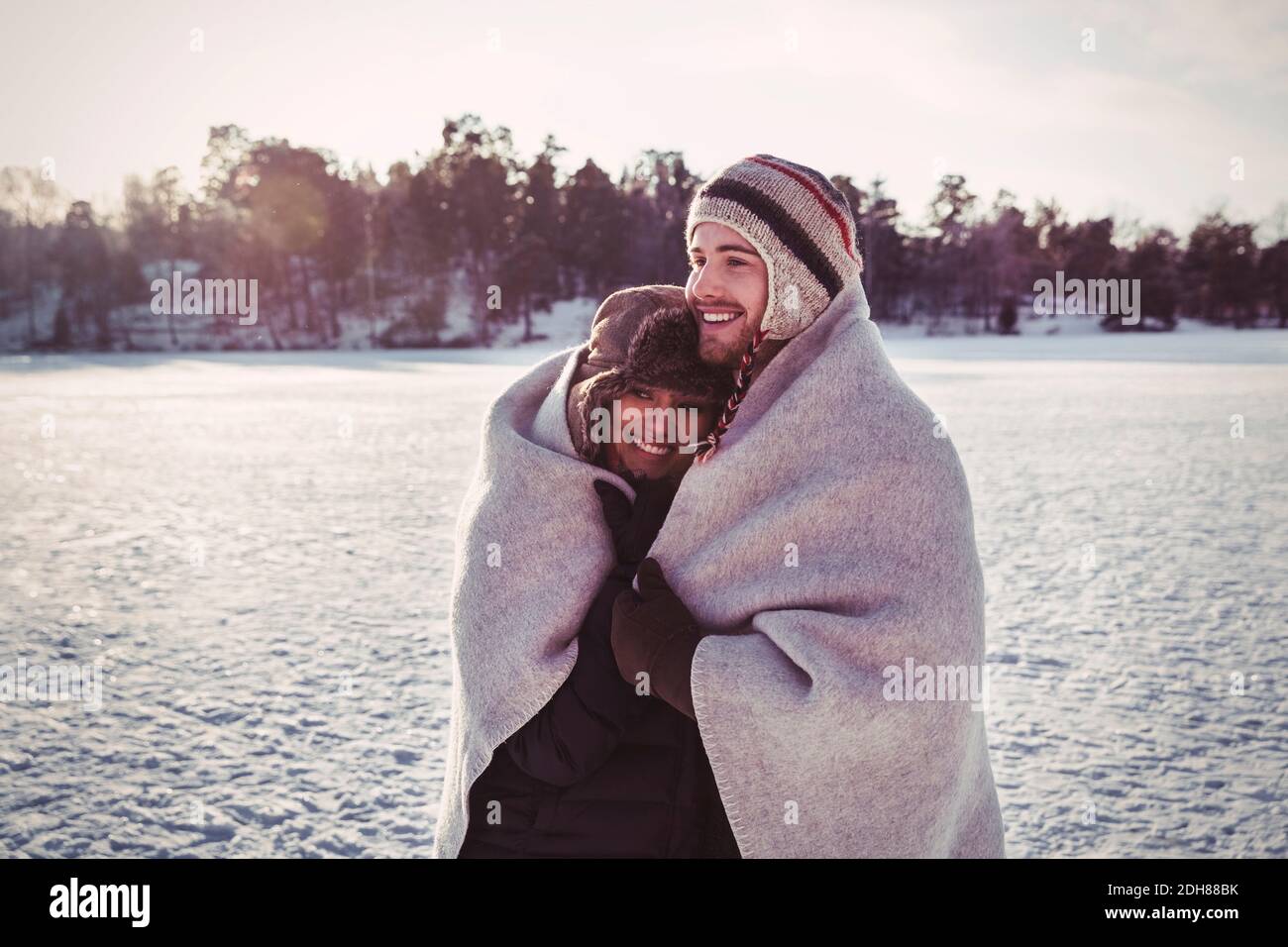 Smiling couple wrapped in blanket while standing on field during winter Stock Photo