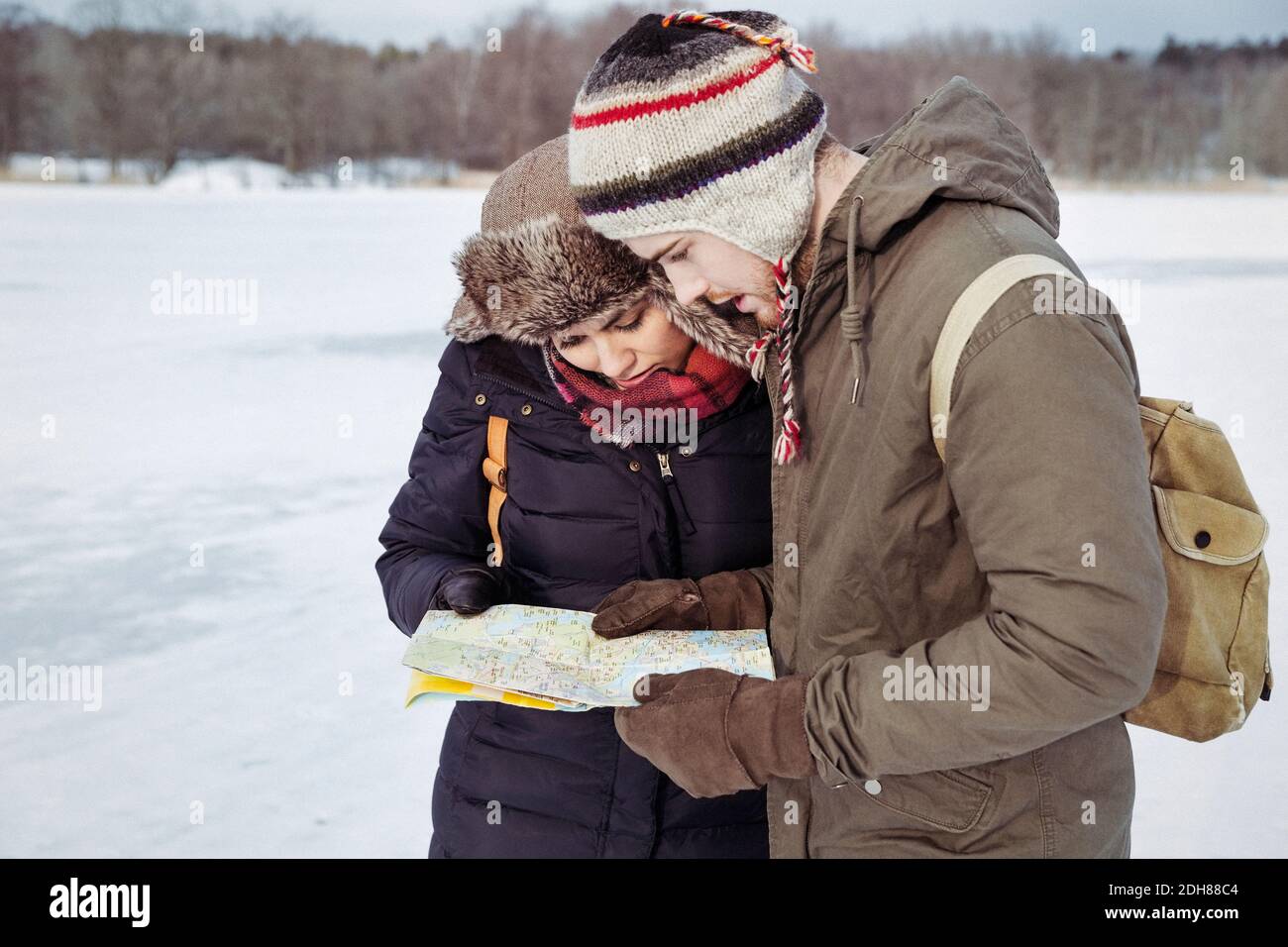 Couple looking at map while standing on field during winter Stock Photo