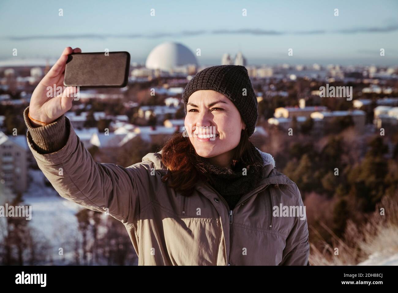 Smiling woman clicking selfie through smart phone during winter Stock Photo