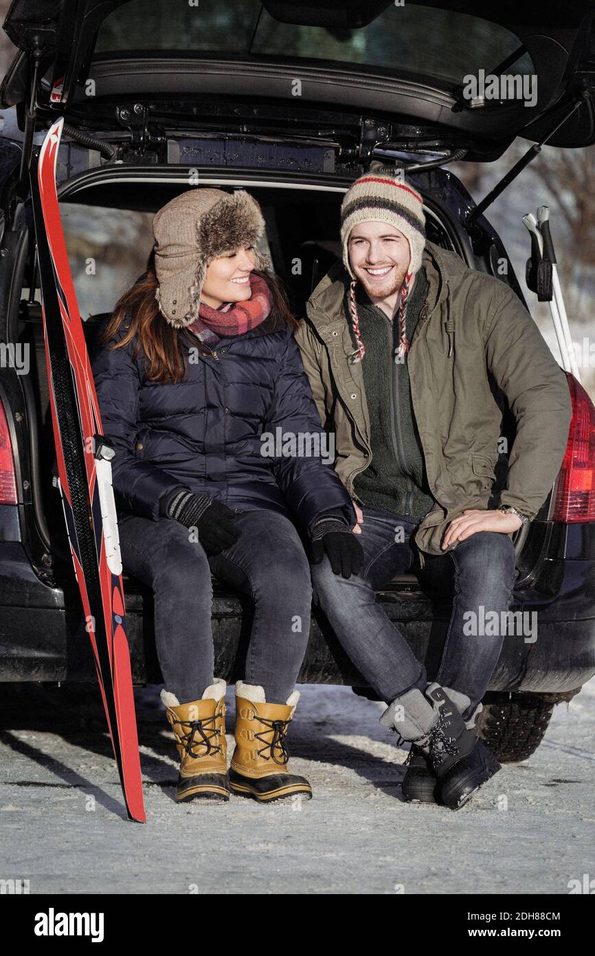 Happy couple talking while sitting on car trunk Stock Photo