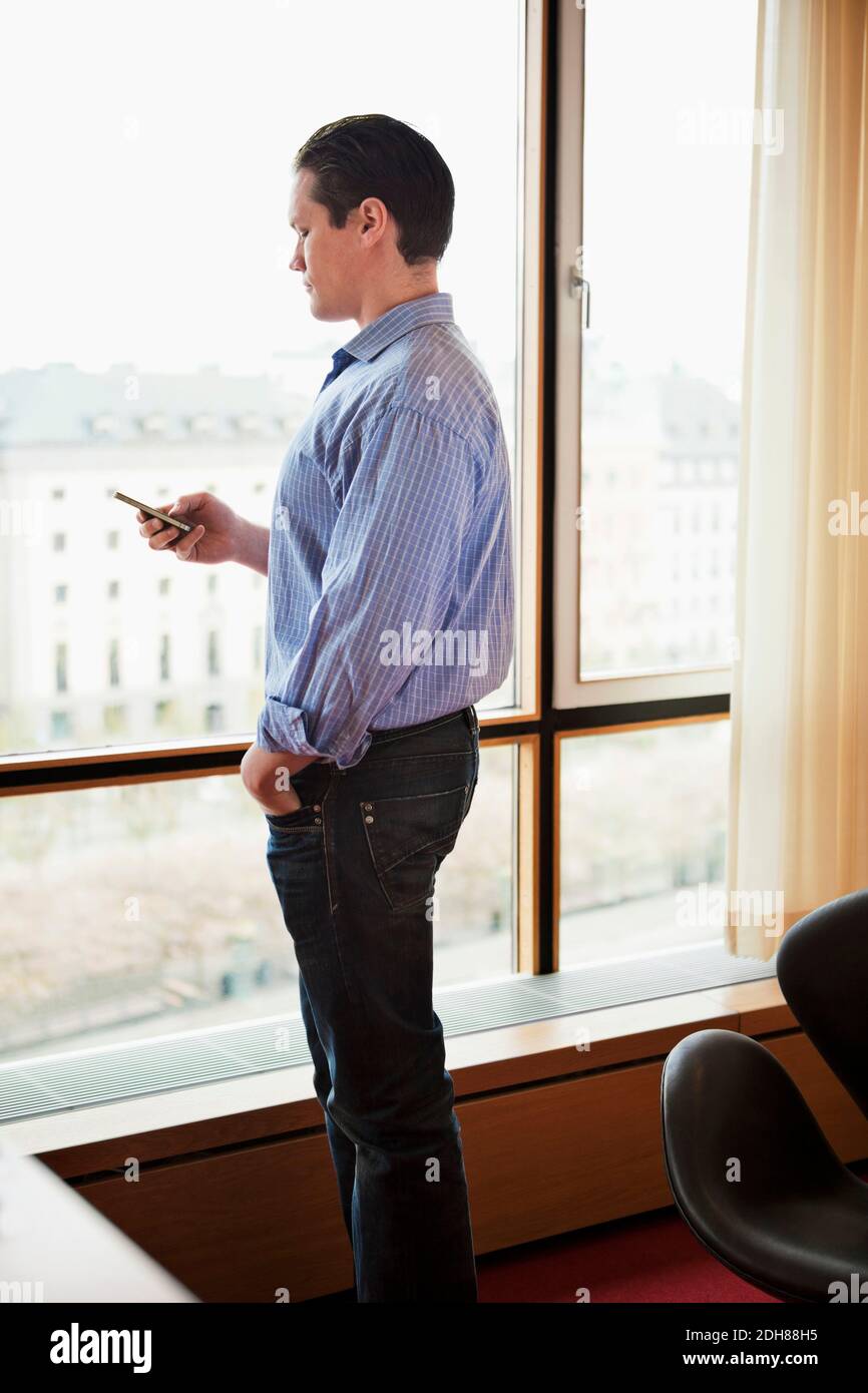 Handsome mid adult businessman text messaging near window Stock Photo