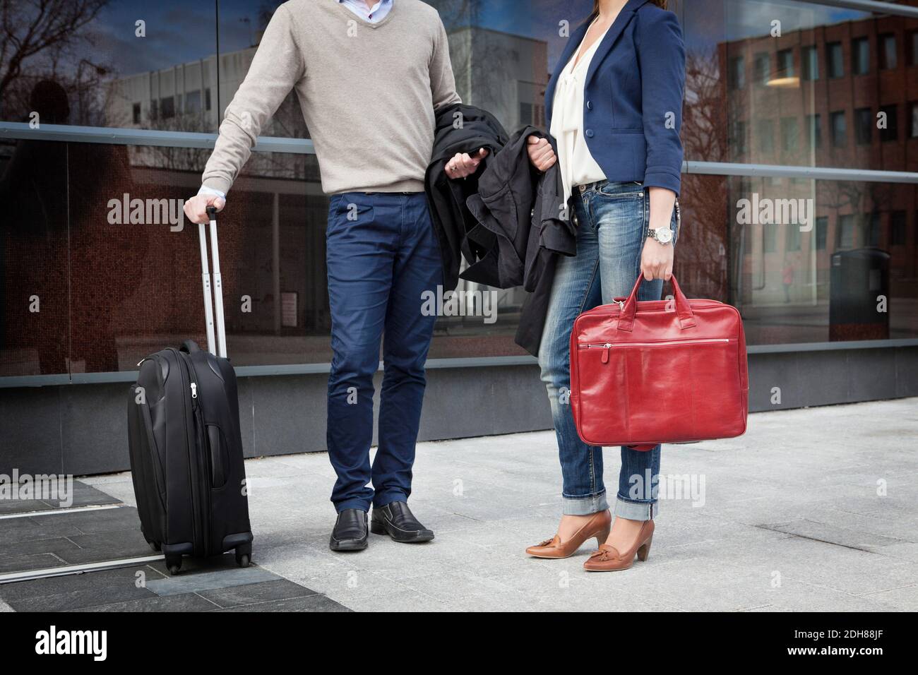 Two friends standing in front of glass building with luggage Stock Photo