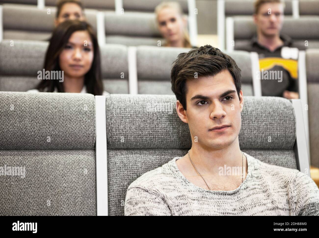 Close up of handsome young man sitting in convention center with friends in background Stock Photo