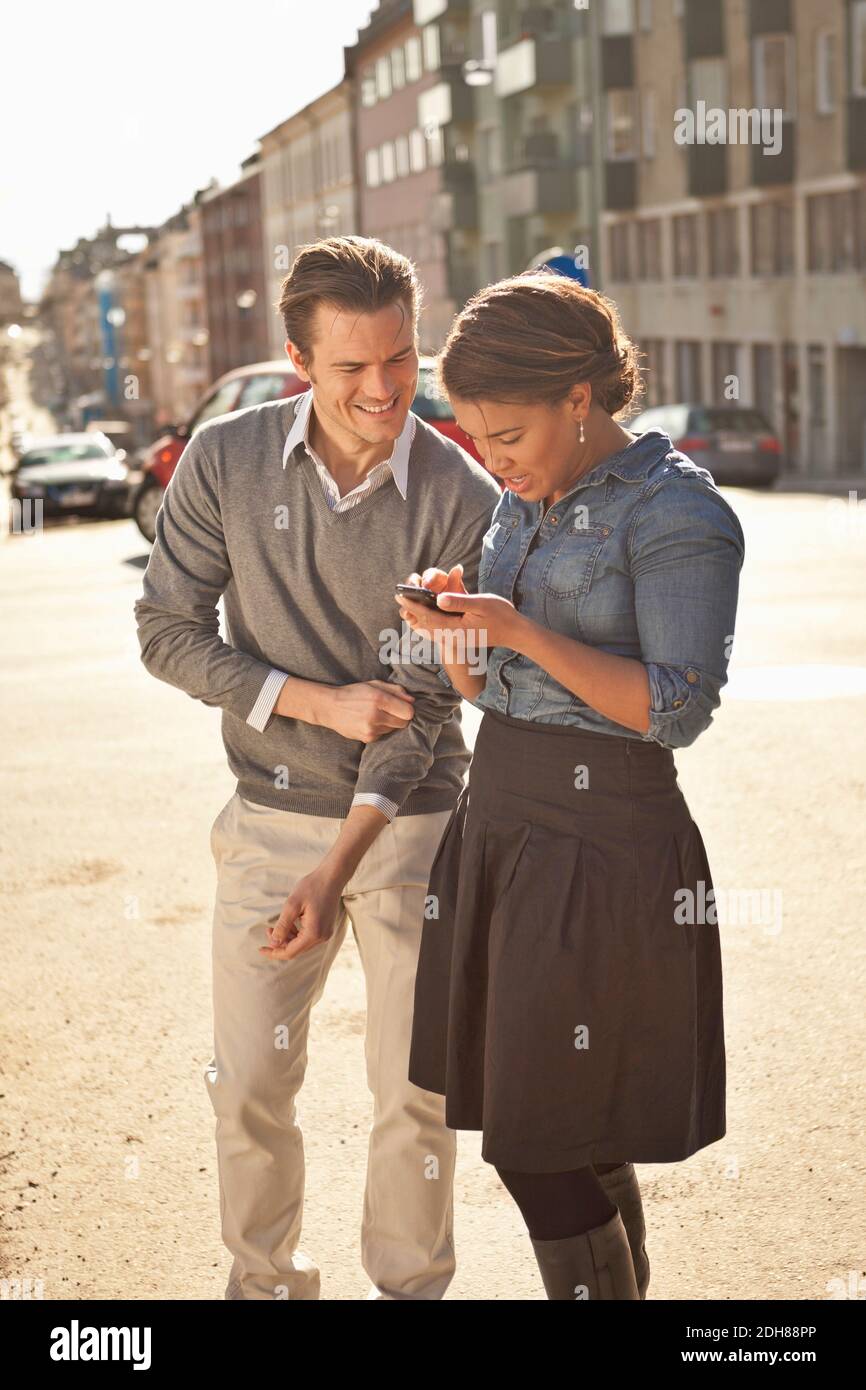 Mid adult friends text messaging on street Stock Photo