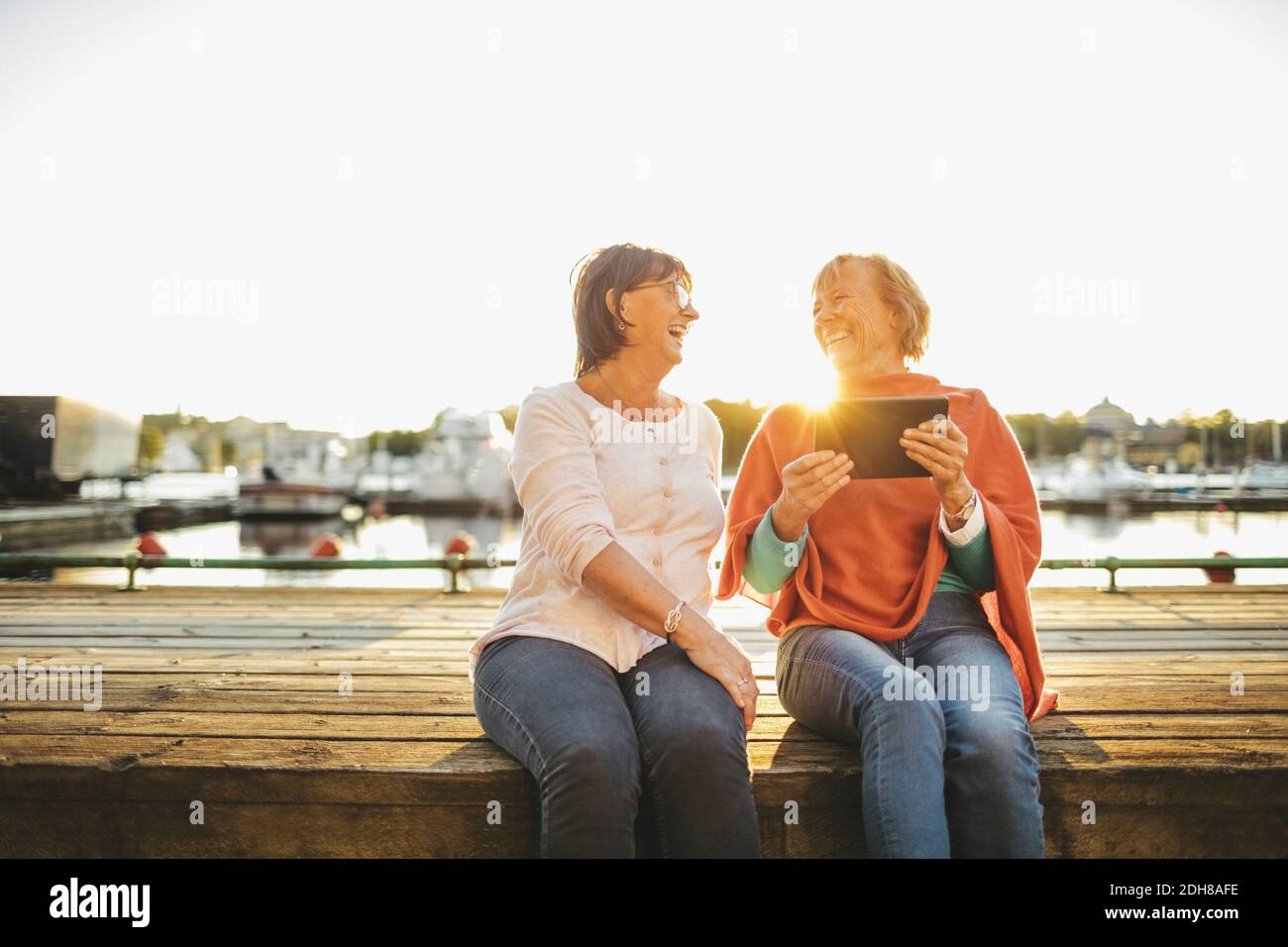 Happy senior woman with female friend holding digital tablet on pier Stock Photo