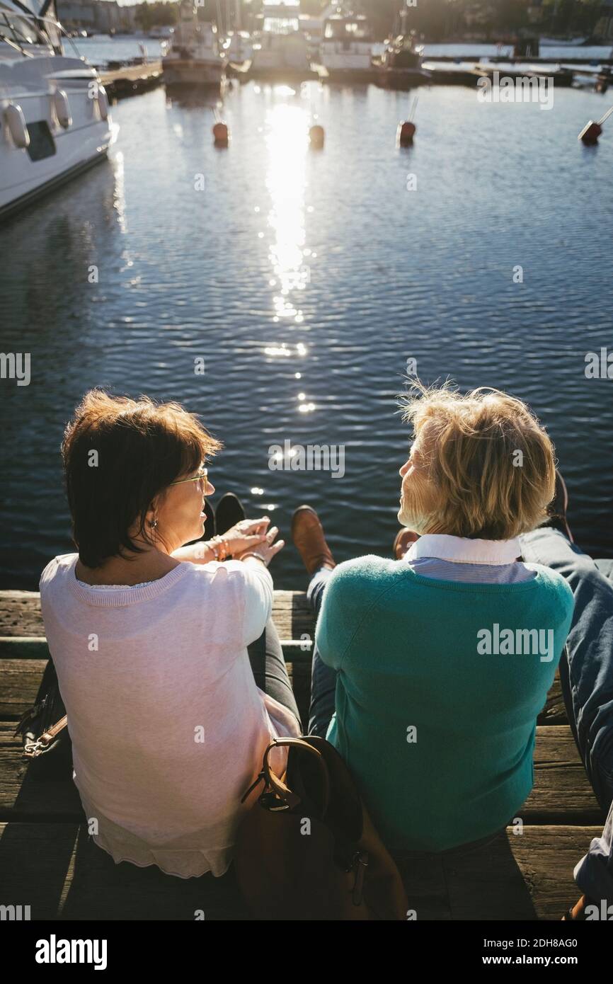 Rear view of senior women talking while sitting on pier Stock Photo