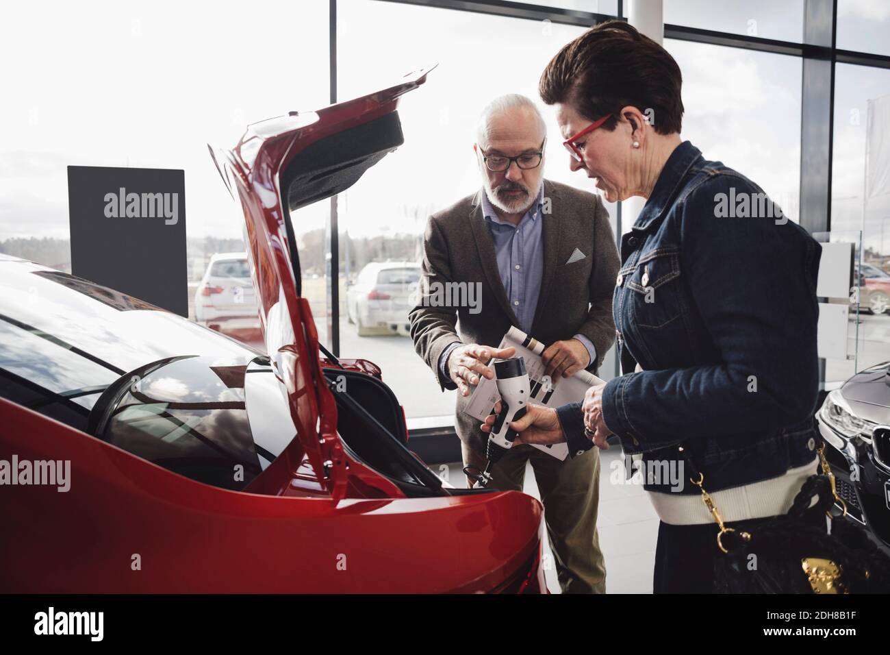 Senior man and woman examining charger of electric car at showroom Stock Photo