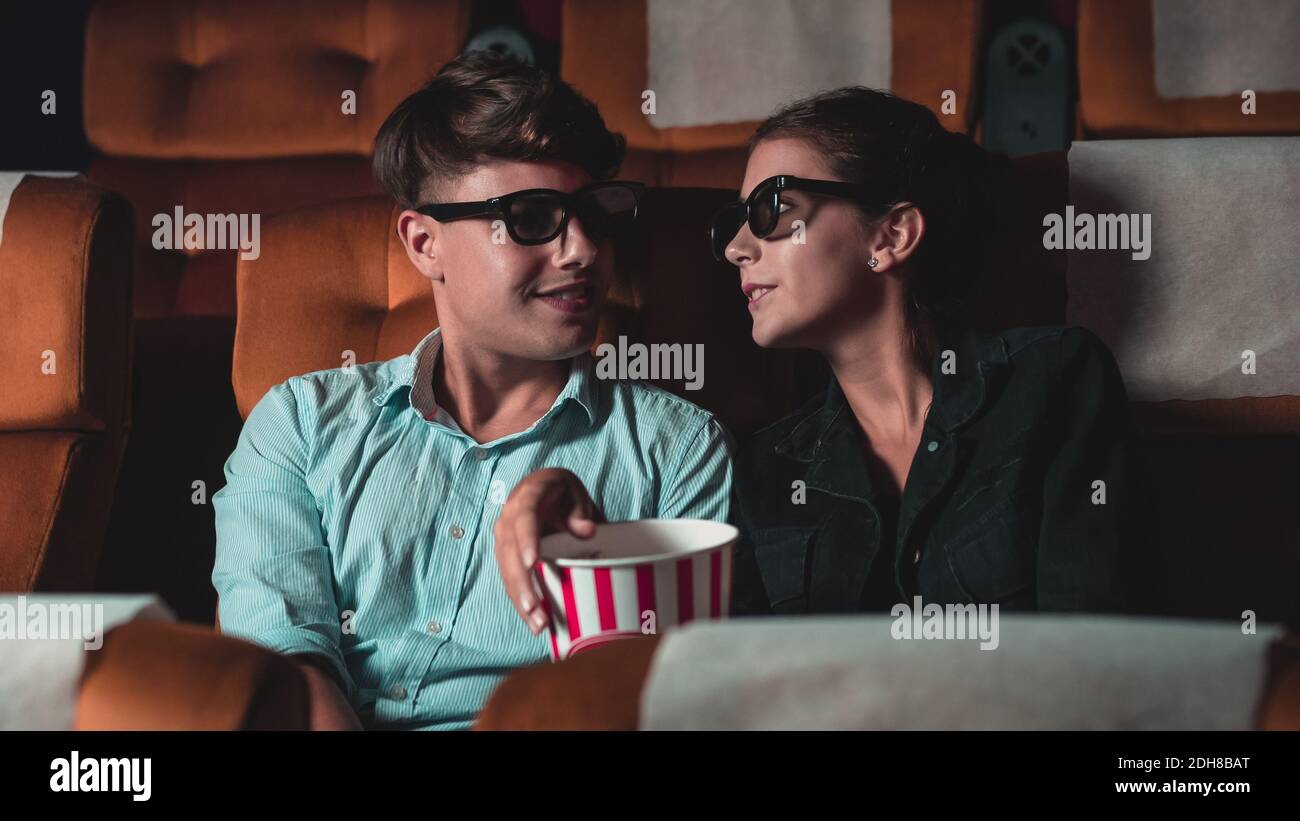 Man and woman in the cinema watching a movie with 3D glasses. with interest looking at the screen, exciting and eating popcorn Stock Photo