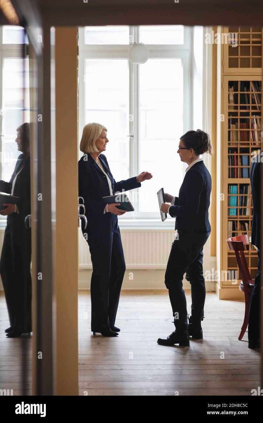 Senior lawyer discussing with female coworker while standing in library seen from doorway Stock Photo