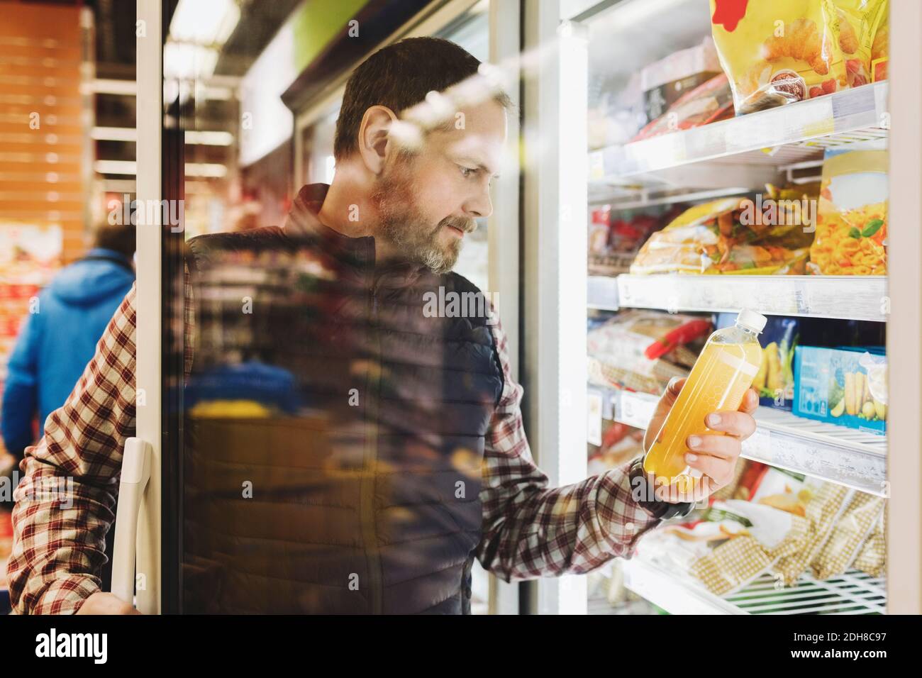 Male customer reading drink label seen through glass door at refrigerated section Stock Photo