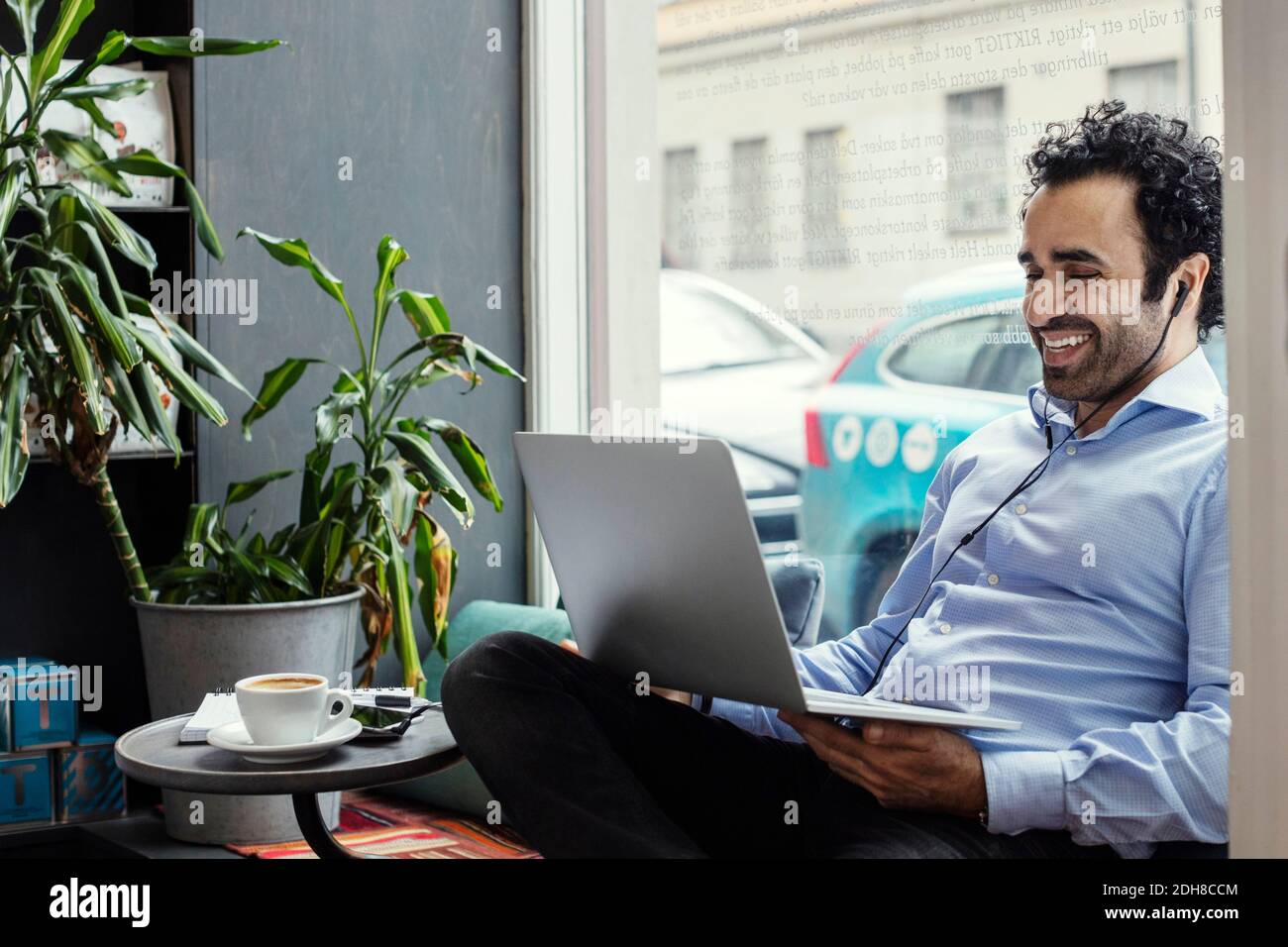 Happy businessman using laptop while sitting by window in creative office Stock Photo