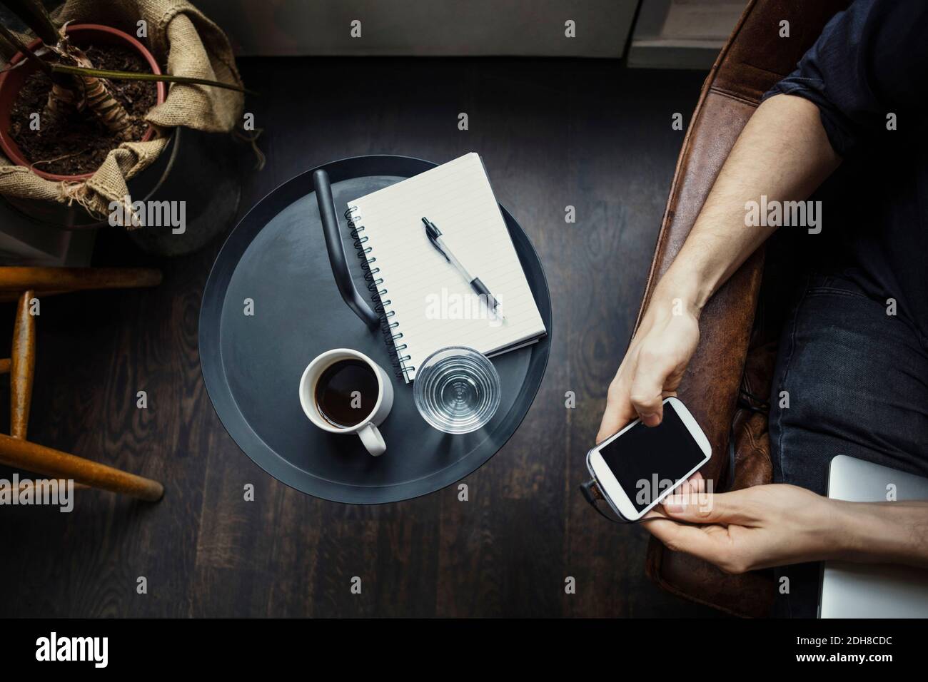 Cropped image of businessman using phone while sitting by drinks and spiral notebook Stock Photo
