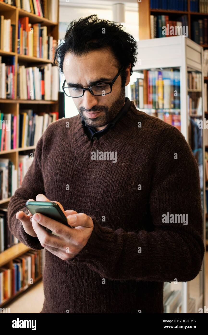 Man using phone while standing in library Stock Photo