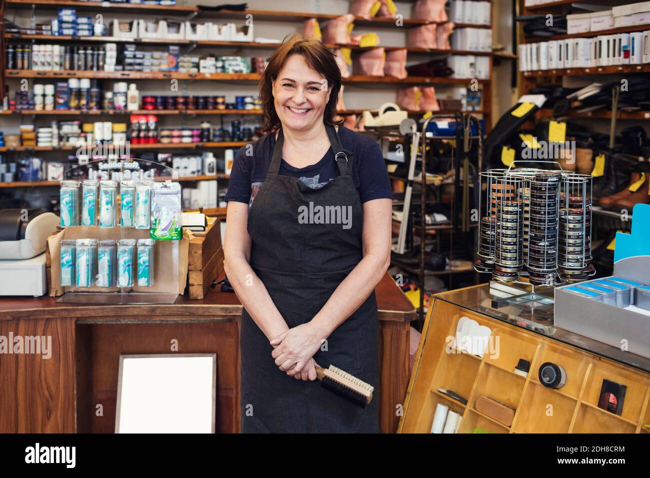 Portrait of happy shoemaker holding shoe brush while standing in shop Stock Photo