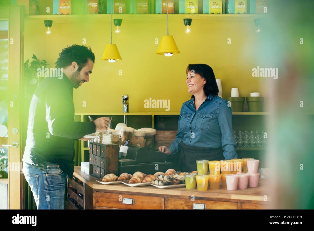 Happy waitress looking at male customer adding sugar in coffee Stock Photo