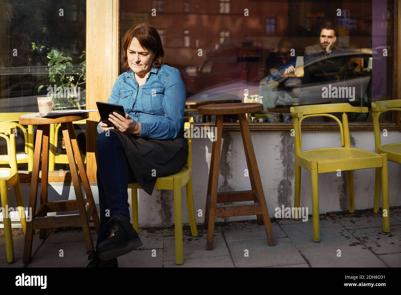 Female owner using digital tablet while sitting at sidewalk cafe Stock Photo