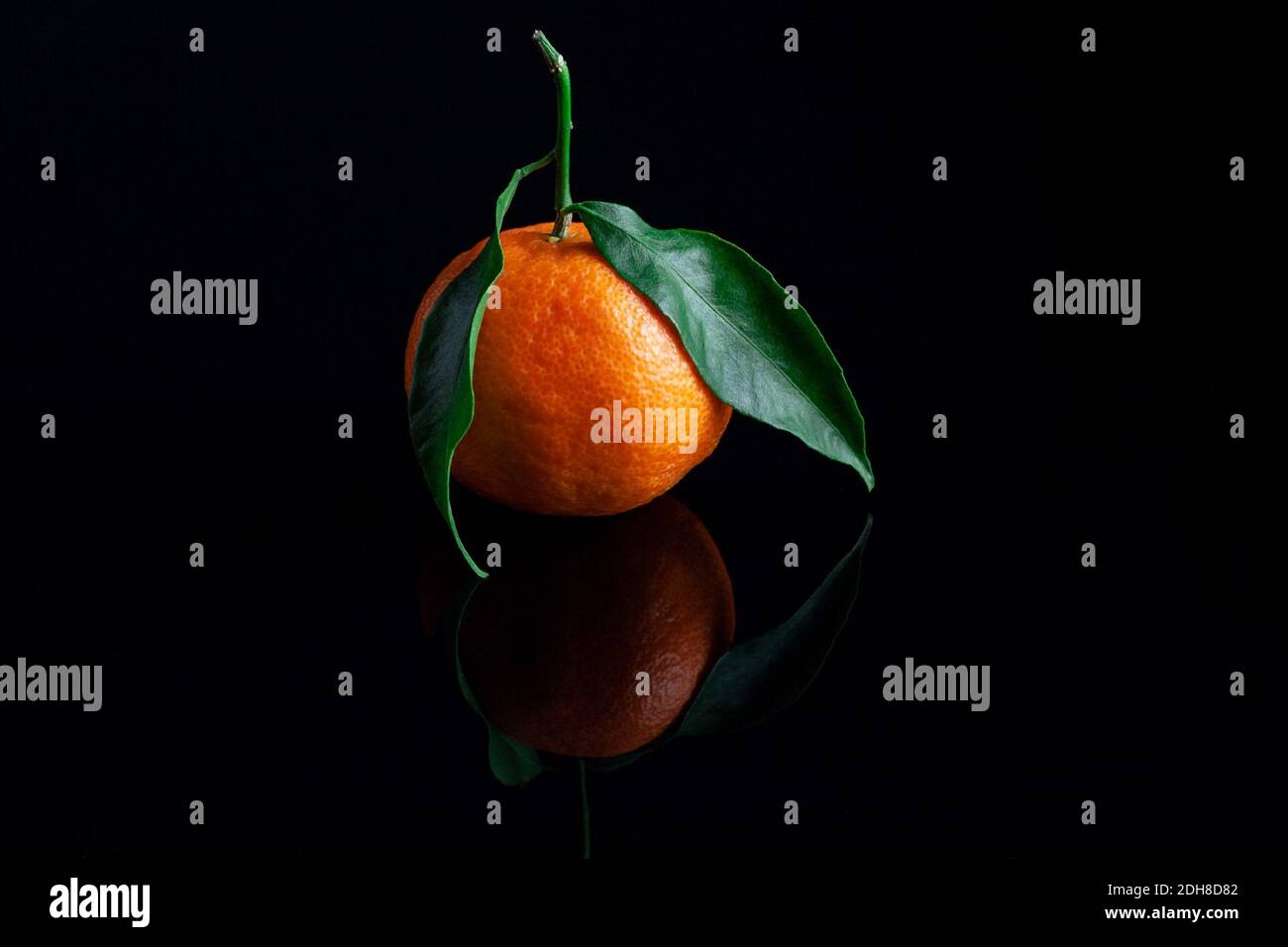 Delicious and beautiful Tangerines with green leaf. Peeled Mandarine orange and Tangerine orange slices on a Dark reflective surface. Stock Photo
