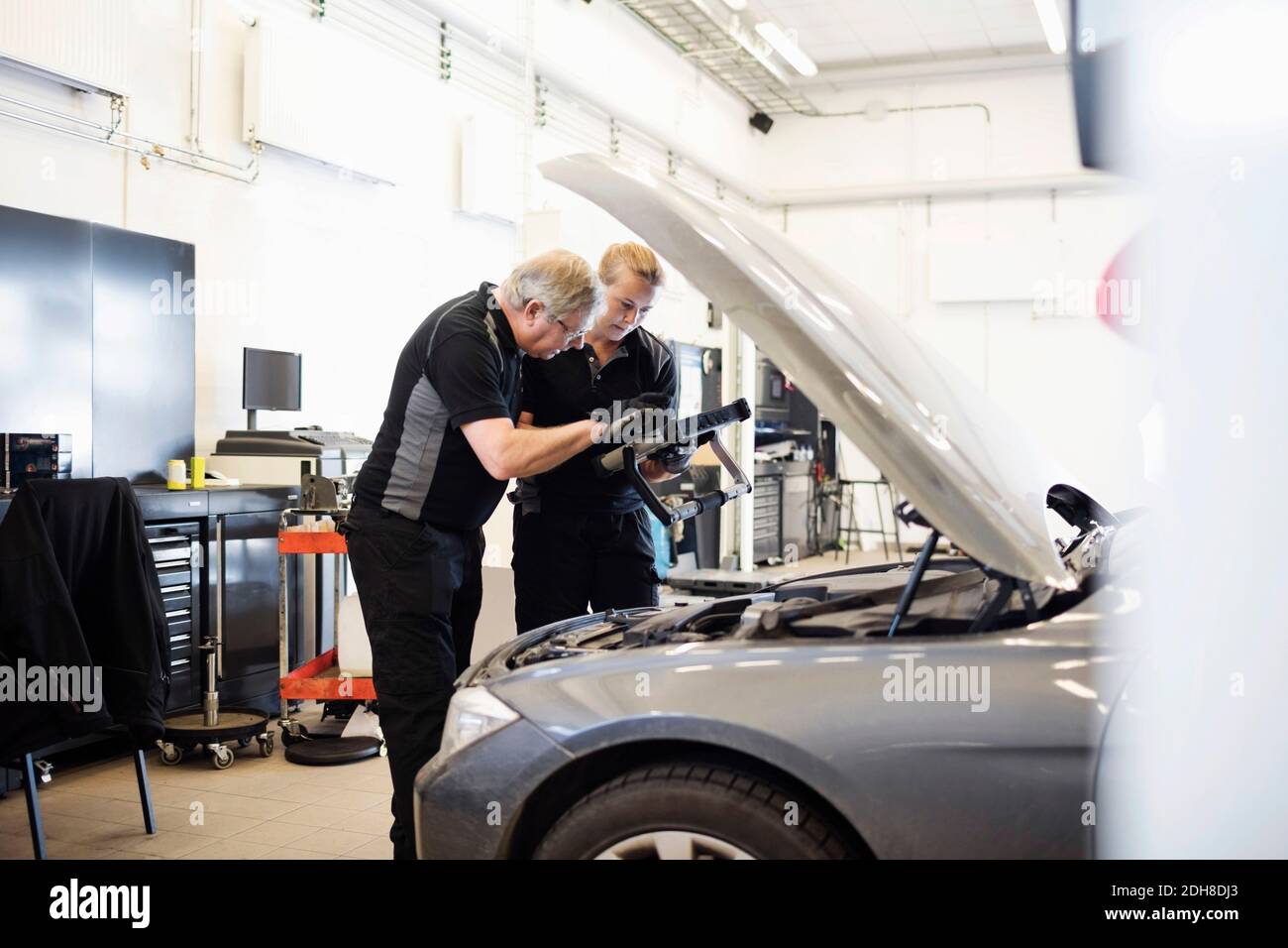 Male and female experts using technology while examining car at shop Stock Photo