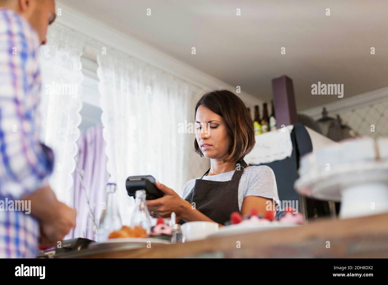 Serious baker using credit card reader while man standing at cafe counter Stock Photo