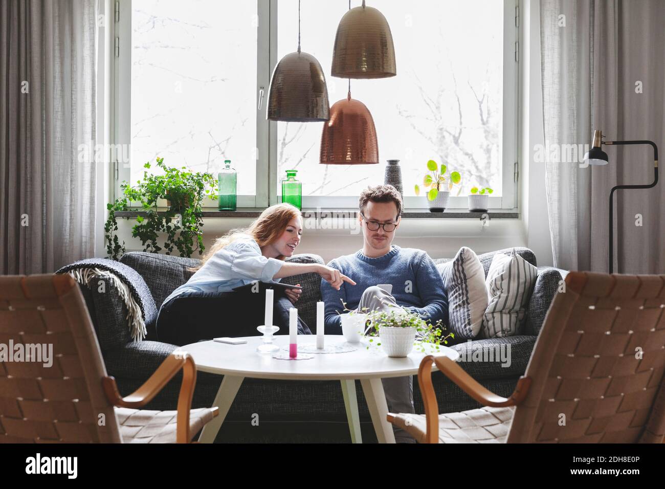 Couple using technologies while sitting on sofa at home Stock Photo