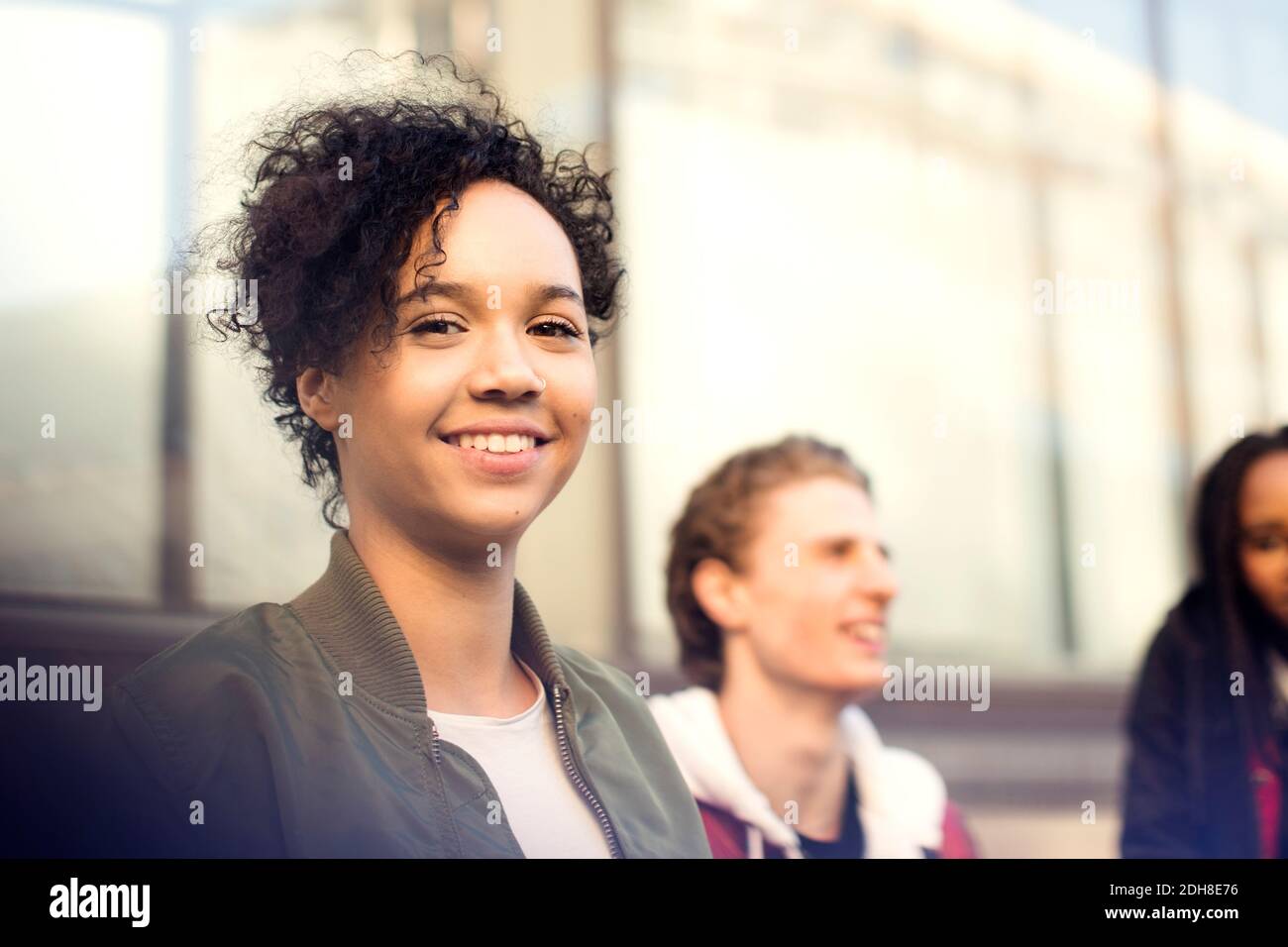 Portrait of smiling teenage girl with short curly hair standing with friends in city Stock Photo