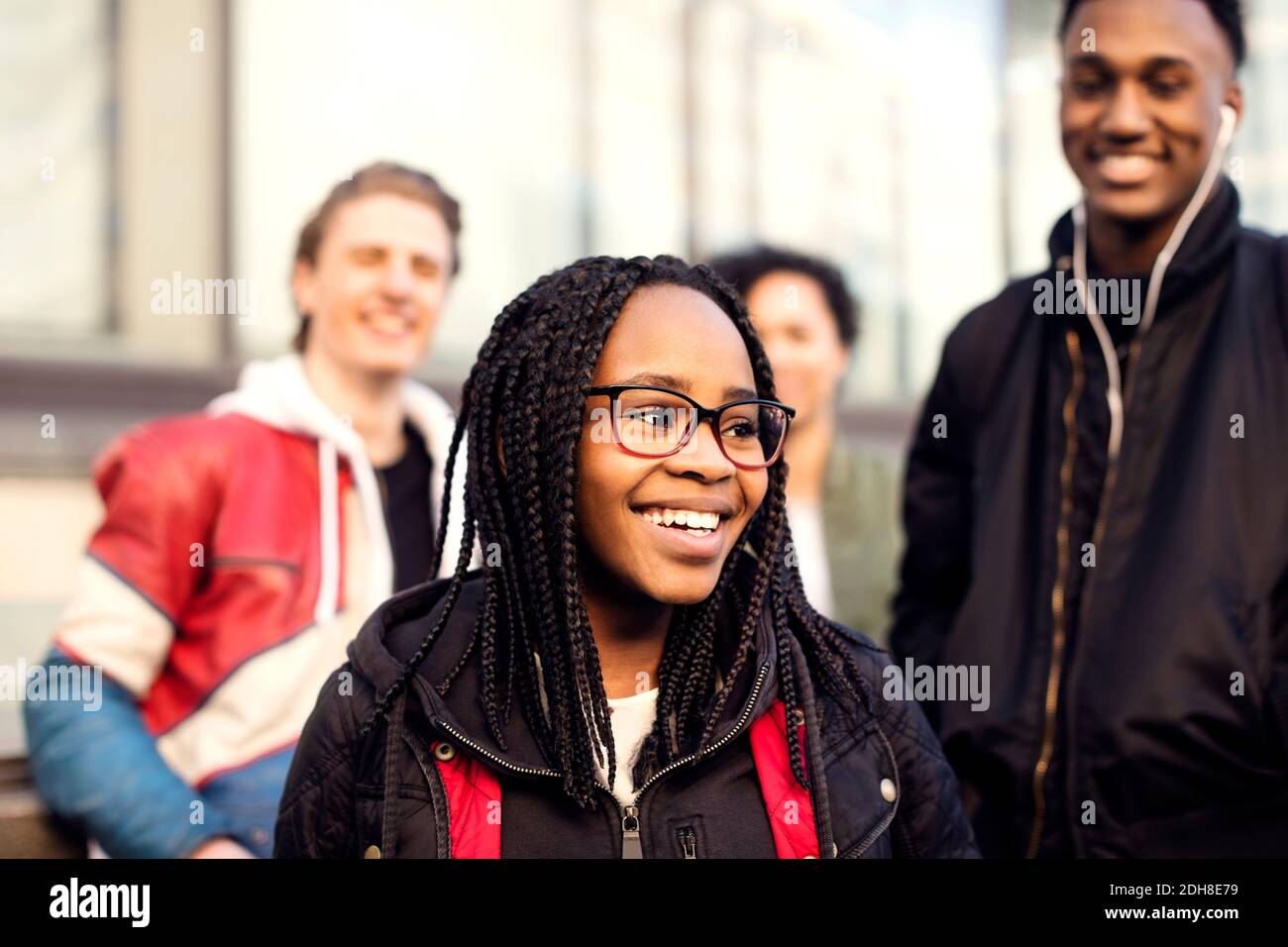 Smiling teenager with braided hair wearing eyeglasses standing against friends in city Stock Photo